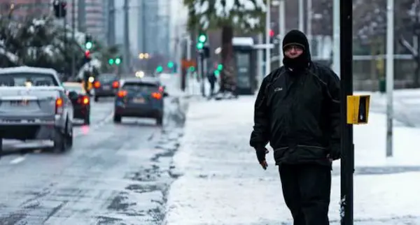 Hombre caminando por el frío extremo de la ciudad con nieve en las calles y vistiendo ropa de abrigo.