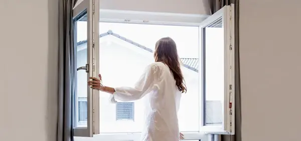 Mujer abriendo una ventana de PVC en su hogar, aislando su casa del extremo frío.